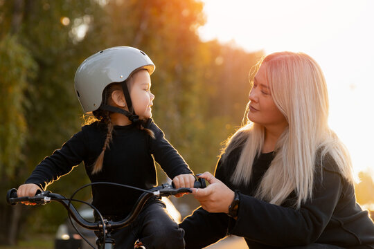Caucasian young girl learns to ride bicycle with supportive female adult in park