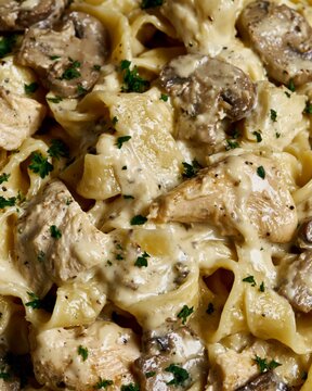 Pasta, chicken, and mushrooms mixing in a rich creamy alfredo sauce, garnished with fresh parsley
