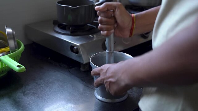 Close-up of hands grinding ingredients with a traditional mortar and pestle in a home kitchen during food preparation.