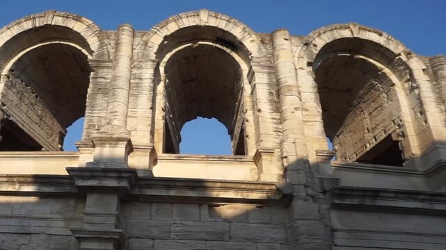 Close view of the ancient Roman Theatre of Arles, featuring monumental stone arches and columns under a clear blue sky in Provence, France.