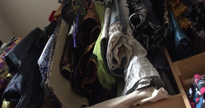 A slow pullback from beneath a rack of colorful Mardi Gras costumes, revealing layers of clothing, fabric, and accessories filling a crowded closet.