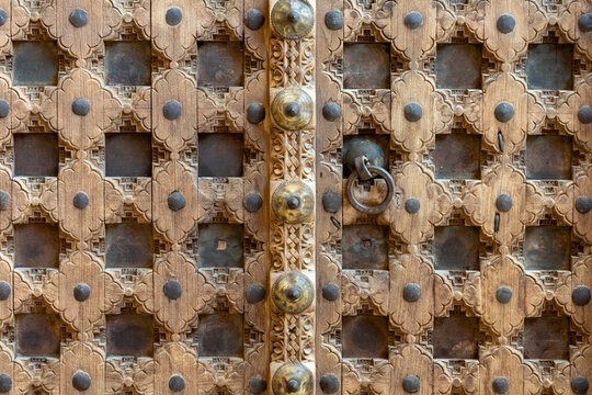 Close-up of a traditional carved wooden door featuring handcrafted details, metal studs and geometric floral ornamentation in Konya, Turkey.