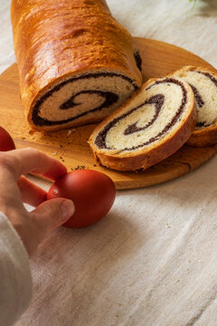 Poppy seed roll on a wooden board, bright dyed eggs. An egg in a hand. Copy space. 