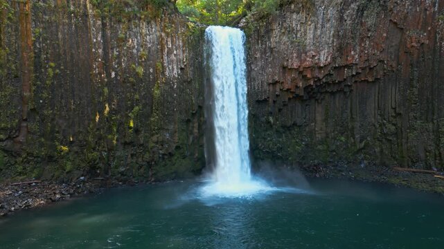 Waterfall flowing into forest pool at Abiqua Falls, Oregon enclosed by basalt cliffs, drone establishing medium orbit right