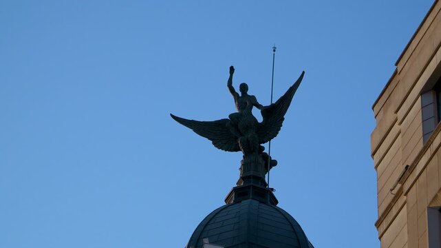 A silhouette of the iconic Winged Victory statue on the Metropolis Building dome against a clear blue sky in Madrid. Suitable for travel documentaries and European city tours.