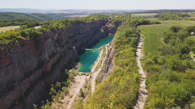 Drone orbit shot circling above emerald flooded lake and steep canyon rock walls at Velka Amerika limestone quarry, Cesky Kras, Czech Republic