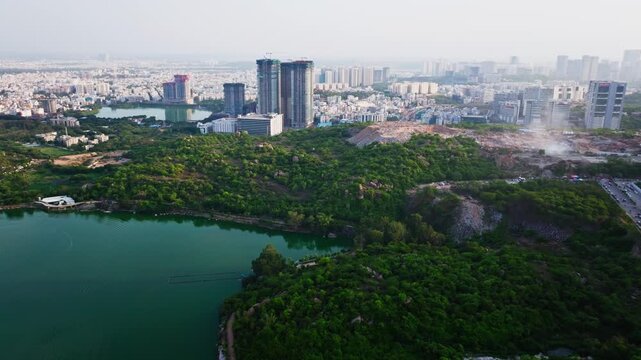 Active construction tower buildings with land clearing dust, buildings, greenery and Durgam Cheruvu at madhapur, serilingampally, hyderabad, telangana, india. day time, push in shot, drone shot, 4k.