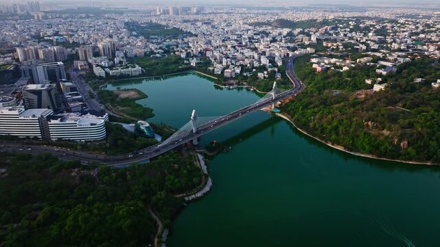 Aerial view of cable bridge with Durgam cheruvu, greenery, traffic flow and buildings at madhapur, hyderabad, telangana, india. day time, push back shot, drone shot, 4k.