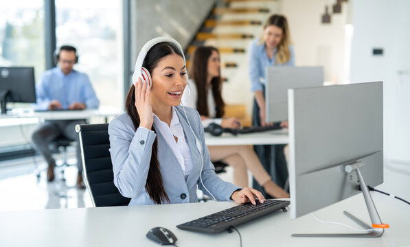 Cheerful female helpline consultant talking on a headset while using a computer