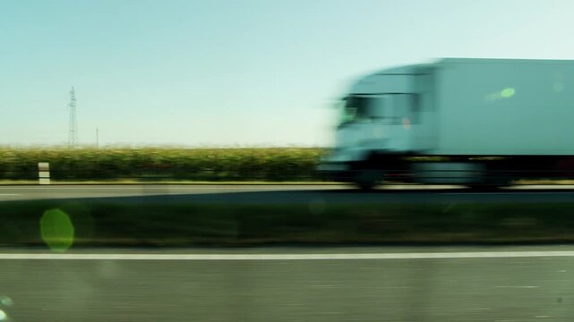 Side view from car window moving fast on blur highway, passing green fields, clear blue sky, distant power line tower, fast blur truck on bright summer day, copy space for text