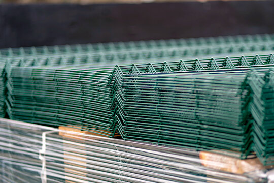 Close-up image showing rows of green metal 3D wire mesh fence panels with stiffening V-bends stacked tightly together on a pallet.