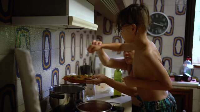 A mother adds pasta to a pot of boiling water while her son tries to help in the farmhouse kitchen