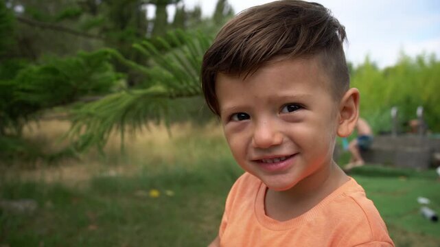 A boy smiles while looking directly at the camera outdoors, Close-Up Portrait Shot