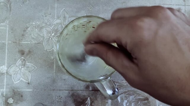 Man uses teaspoon to stir medicine in cup. Person hand stirring liquid content glass cup small spoon medicine preparation drink mixing close up view above kitchen table background