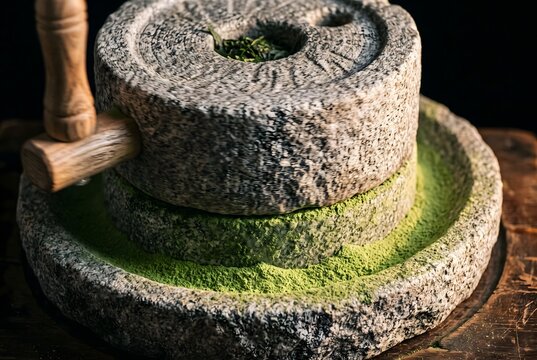 Close-up of a traditional granite stone mill slowly grinding tencha into matcha, fine bright jade powder emerging from the seam between the stones and forming a soft ring at the base.