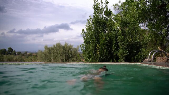 A boy swims happily in an infinity pool and smiles at the camera before climbing out and standing at the edge, Static Shot