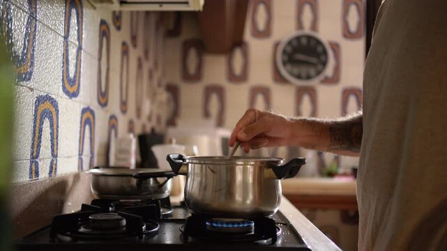 A man's arm reaches into frame to stir tomato paste in a pot on the stove before exiting the shot, Static Shot