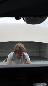 Vertical screen man tries to fix a broken vehicle under the open hood using simple tools and personal effort while working independently to get the car running once again