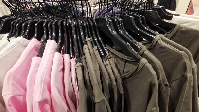 Clothing garments of various colors hanging on black hangers in a retail store displaying casual apparel for purchase on a circular clothing rack