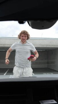 Vertical screen cheerful car owner jumps with excitement beside the open hood after successfully repairing the vehicle himself celebrating a satisfying mechanical victory