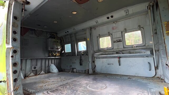Interior view of abandoned military transport helicopter cargo bay cabin with metal walls, floor, and ceiling, showing exposed structure, windows, and open door