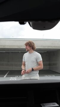 Vertical screen stranger walks up to a parked car scratches its paint with a sharp object and exits the garage after intentionally committing a malicious act of vandalism
