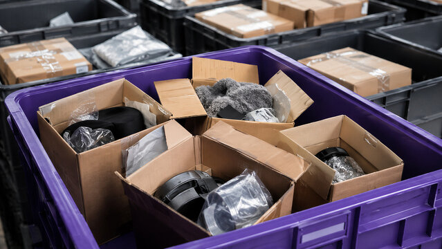 Opened cardboard boxes with returned products in purple plastic bin at warehouse. E-commerce return after Black Friday and Cyber Monday sale. Reverse logistics and inventory sorting concept