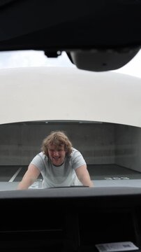 Vertical screen confused car owner stares under the open hood and struggles to understand the breakdown feeling helpless because he does not know how to repair the engine
