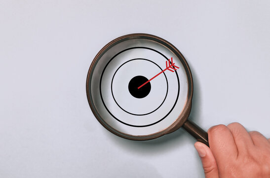 Target board inside of magnifying glass for focus business objective on blue background and copy space.