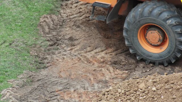 Orange heavy construction equipment vehicle wheel churning mud at construction site creating deep tire tracks, ground work moving earth and rocks