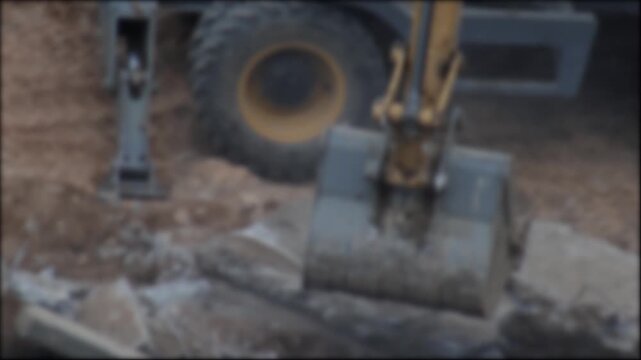 Excavator bucket breaking concrete slabs and moving earth at construction site. Heavy machinery operation during demolition, ground preparation, and civil engineering work, blurry, copy space