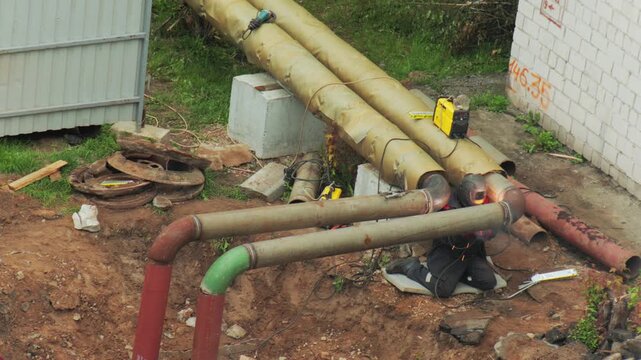 Worker welding metal heating pipes outdoors during pipeline construction activity, bright spark of welding process visible, industrial repair scene with exposed utilities
