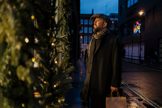 A bearded man looks at a festive shop window during winter evening
