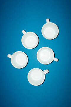 Five empty white porcelain coffee cups on a blue background