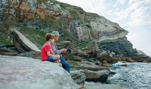 Grandfather and grandson fishing together at the sea sitting on rock