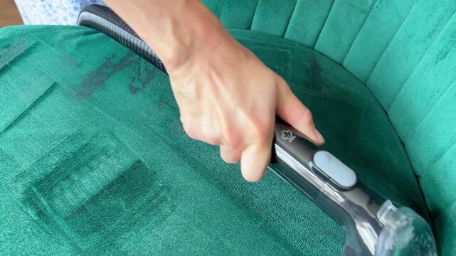 Deep cleaning green velvet armchair with upholstery extractor vacuum. Housekeeping, furniture care, satisfying cleaning, and professional upholstery services.