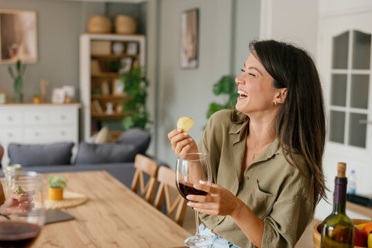 Beautiful woman laughing while holding wine glass in kitchen