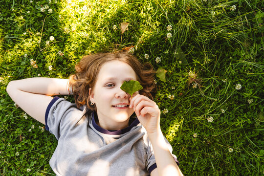 A smiling girl holds a ginkgo leaf over her eye on the grass