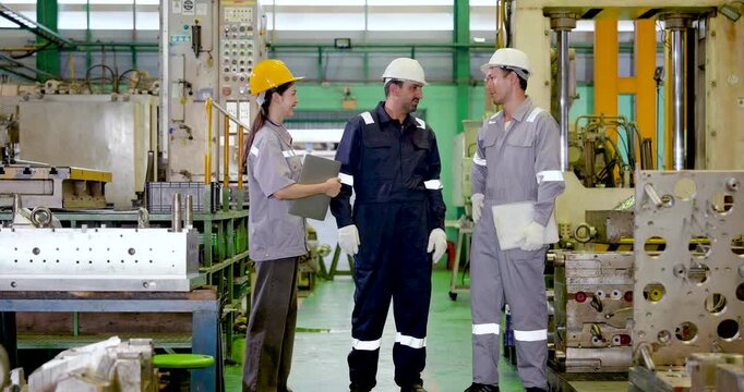 Three adult factory workers talk beside machine station, coordinating production plan, technical communication and workforce collaboration for efficient operation in slow motion