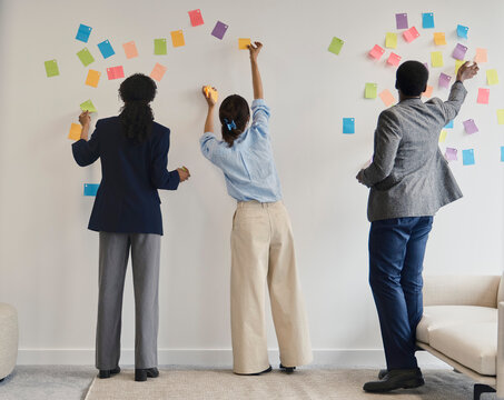 Colleagues place sticky notes on an office wall during a meeting