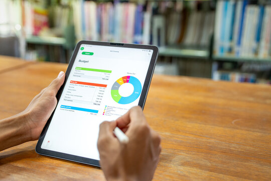 Extreme closeup of hands holding tablet screen showing personal monthly budget planner application with colorful pie chart and expense tracking list