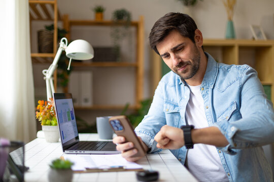 Professional using smartphone and smartwatch for time management at home office