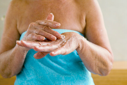 Senior woman wrapped in towel, applying lotion in hands, mid section, close-up