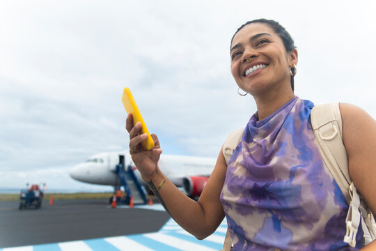 Smiling woman holding smartphone at airport runway before boarding