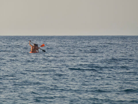 Two people paddling on an orange kayak in deep blue sea ocean waters during calm summer day along Marinello coast near Tindari in Oliveri, Sicily island, Italy.