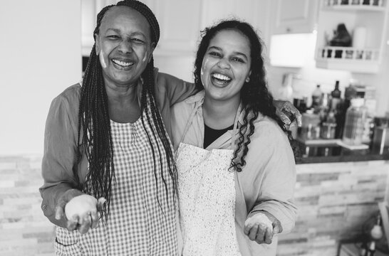 Happy african mother and daughter preparing together bread at home during autumn holidays - Family women having fun cooking together - Main focus on girl face - Black and white editing