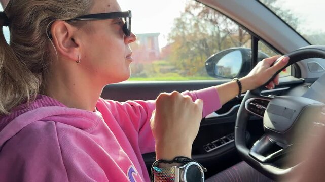 Woman driving, young female driver holding steering wheel in bright sunlight. Static side view shot.