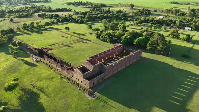 Cinematic aerial footage of the historic Jesuit Missions ruins surrounded by lush green grass in Trinidad, Paraguay.