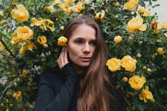 Young woman posing gracefully amidst vibrant yellow roses in a lush garden setting