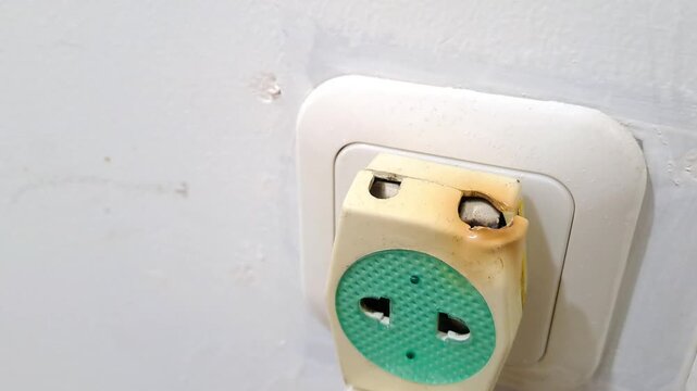 Close-up of a dangerous burnt electric socket adapter plugged into a wall outlet. Electrical hazard, short circuit safety hazard, and risk stock photo.